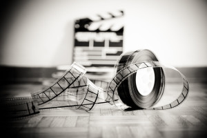 35 mm cinema film reel and out of focus movie clapper board in background on wooden floor in vintage black and white